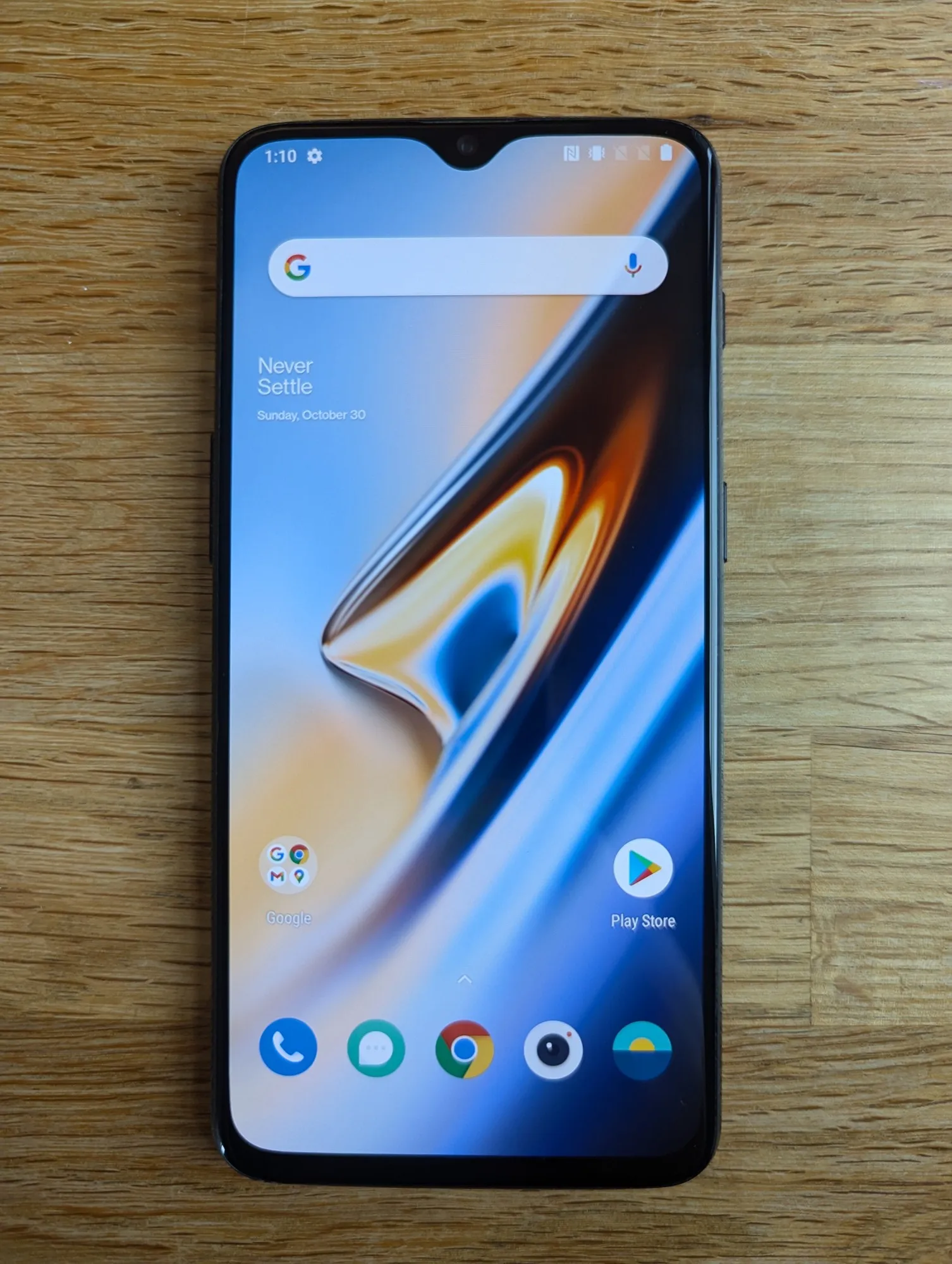 An Android phone from 2018 lying face-up on a wooden desk, showing its home screen.