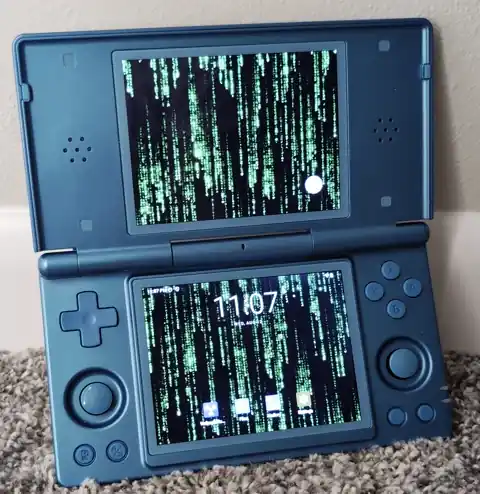 An Anbernic RG DS open on a desk with an animated Matrix-style live wallpaper running on both the top and bottom screens.